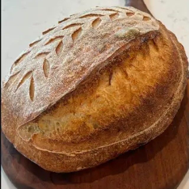 Freshly baked sourdough loaf scored with a wheat pattern